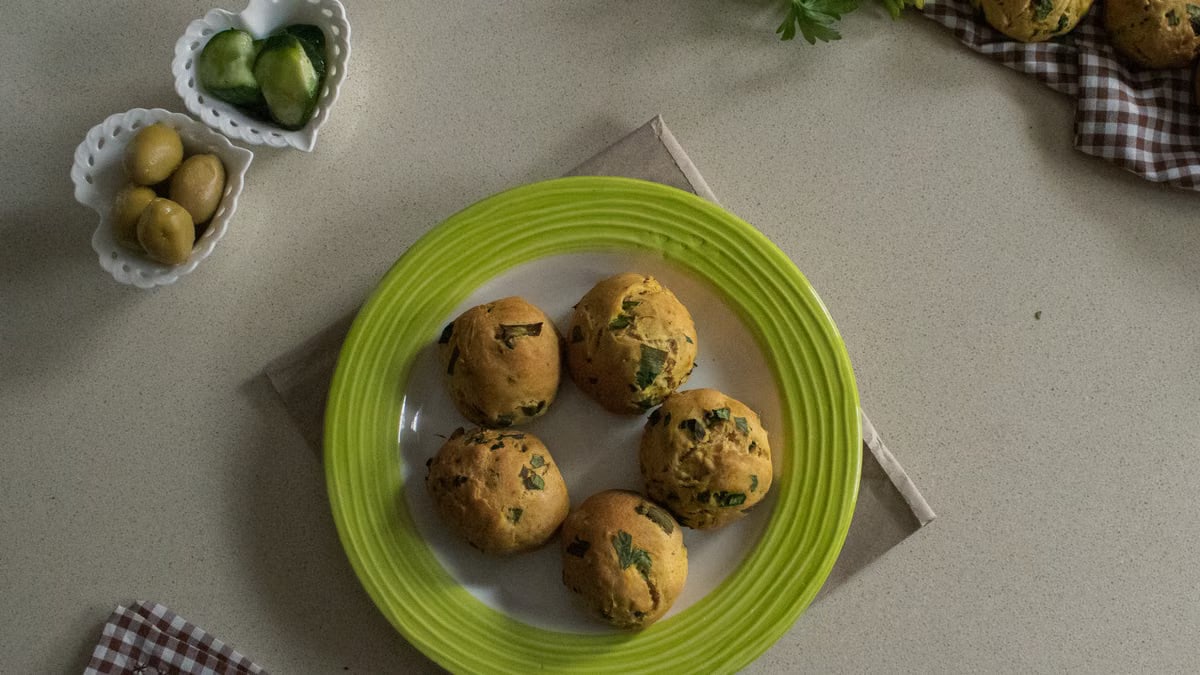 Plate of homemade savory muffins with herbs, served with cucumber and olives.
